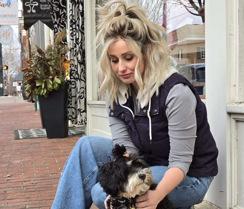 Felicia Delaney smiling while sitting with a Bernedoodle she trained at HappyDoodleFarm.com, representing her multifaceted life as a beauty enthusiast, small business owner, wig influencer and pet lover.